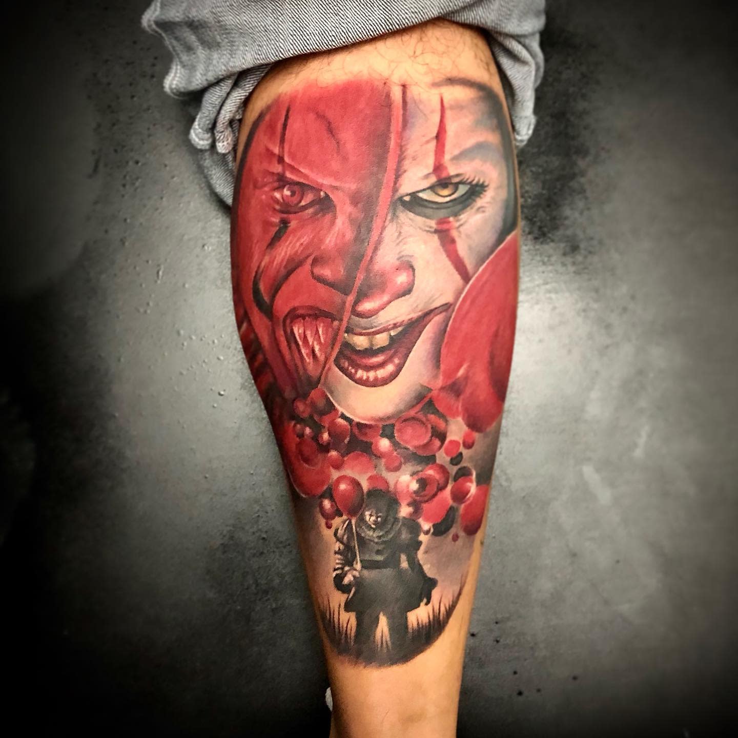 Pennywise tattoo with red tones and balloons, featuring his sinister smile and a shadowy figure